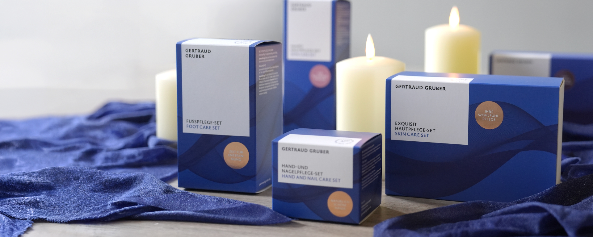 Gertraud Gruber Weihnachts-Sets in festlicher blauer Verpackung, stimmungsvoll arrangiert mit einer brennenden Kerze.